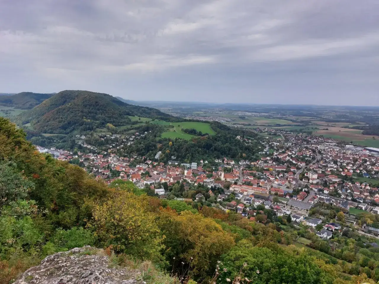 Blick von einem Felsen auf Heubach, das sich ins Tal schmiegt. Ein Wanderer genießt die Aussicht auf die herbstliche Landschaft und die Stadt.