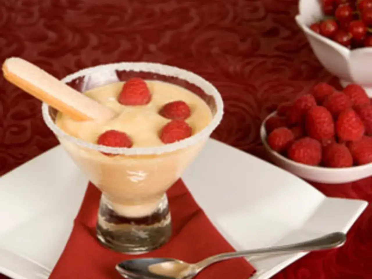 Cremiges Zabaione-Rezept mit frischen Himbeeren und Löffelbiskuit, serviert in einem Glas mit Zuckerrand.