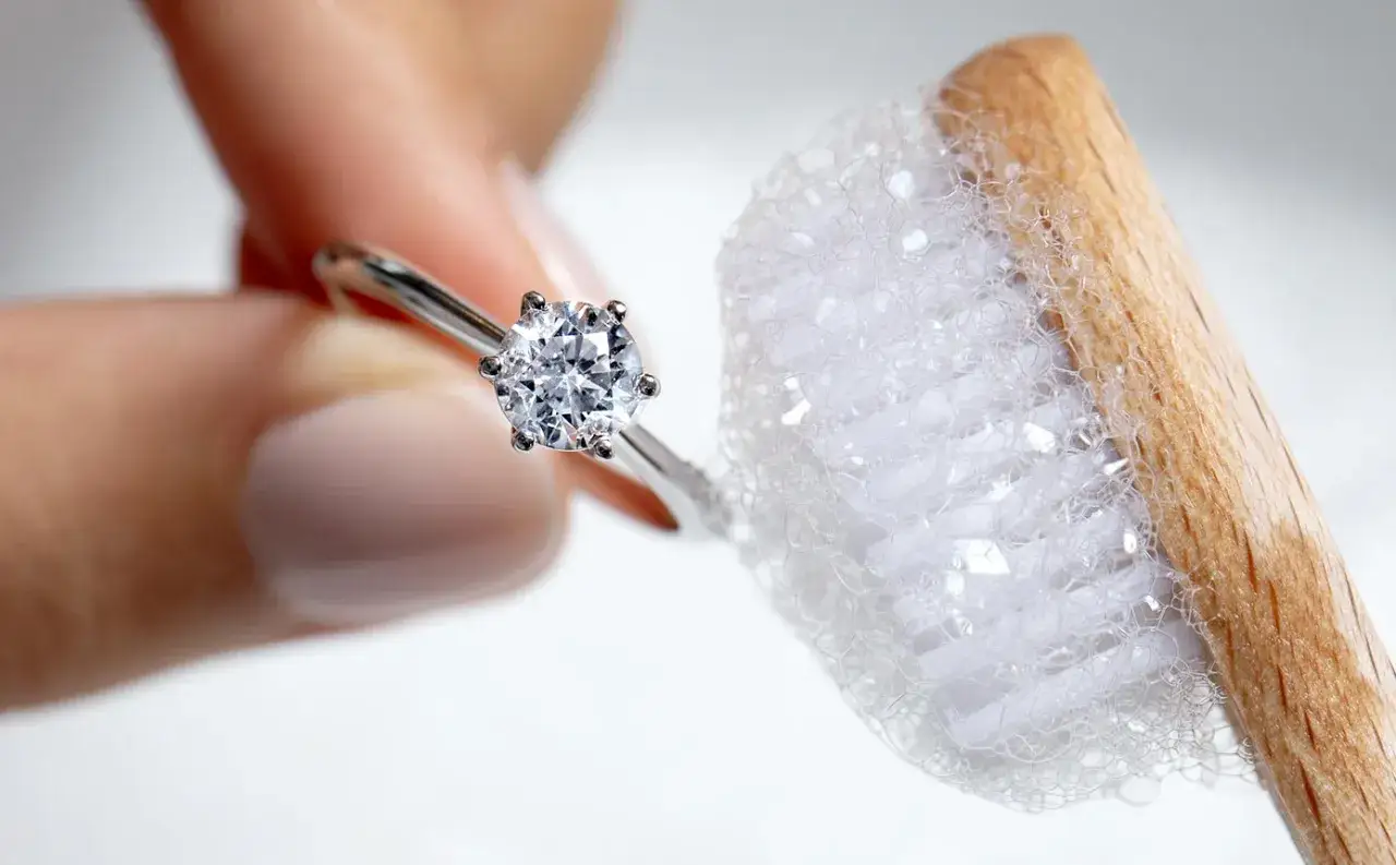 Une bague avec un diamant est tenue pr&egrave;s d'une brosse &agrave; dents savonneuse, montrant comment nettoyer des diamants pour leur redonner leur &eacute;clat.