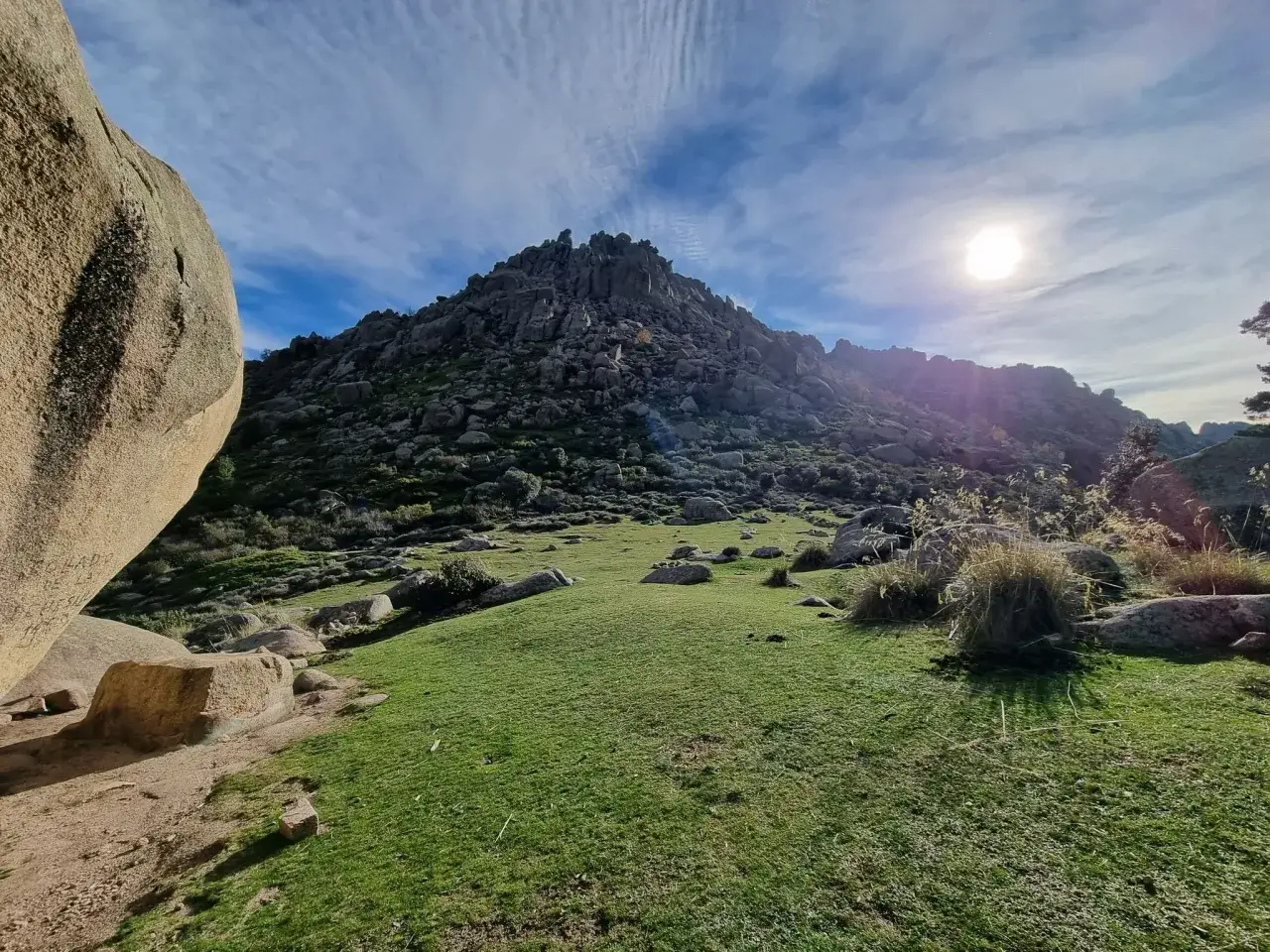 Impresionante paisaje rocoso y verde en la ruta Soto del Real. El sol brilla entre nubes finas.