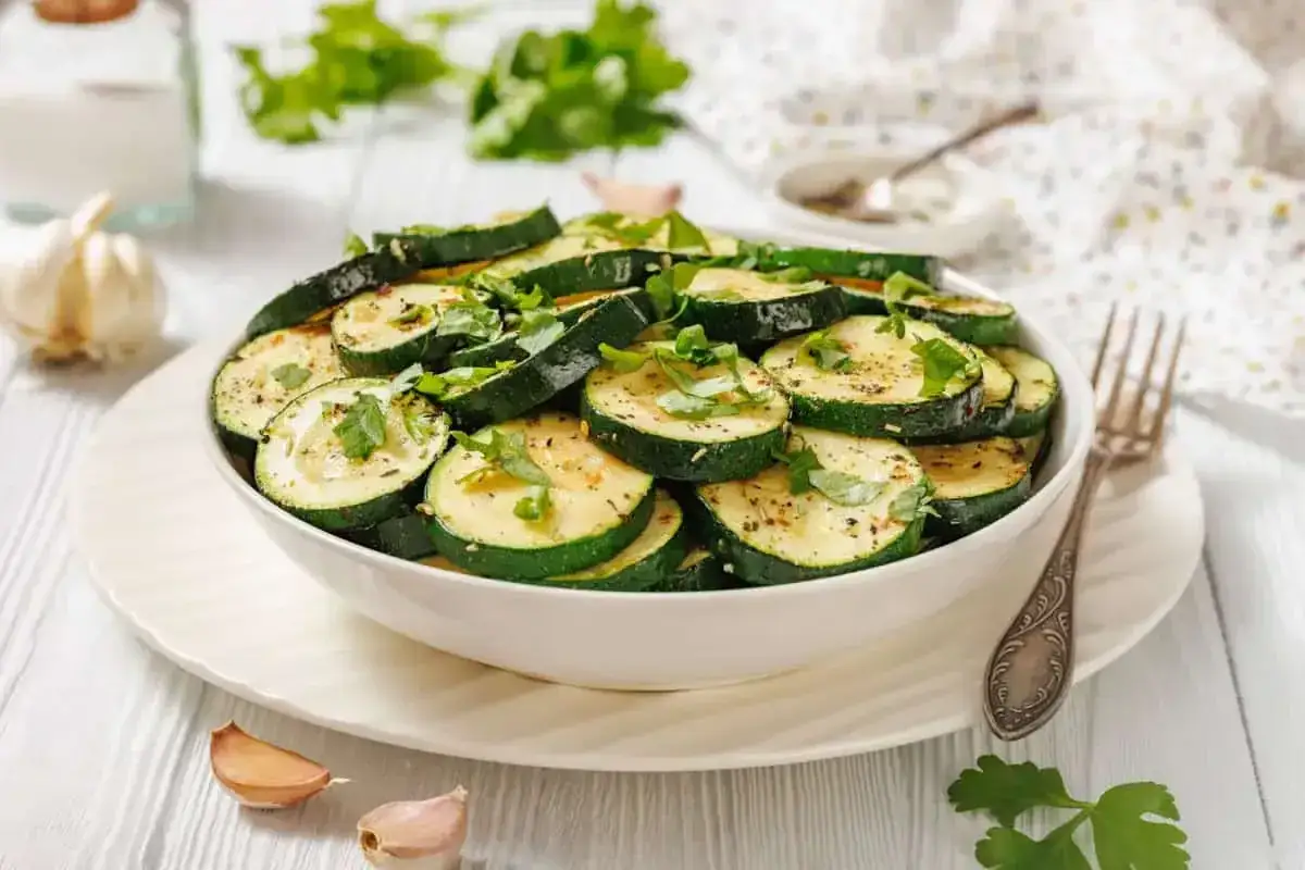 Tranches de courgettes grill&eacute;es, garnies d'herbes fra&icirc;ches, un plat d'&eacute;t&eacute; raffin&eacute;, servi dans un bol blanc avec de l'ail et du persil &agrave; proximit&eacute;.