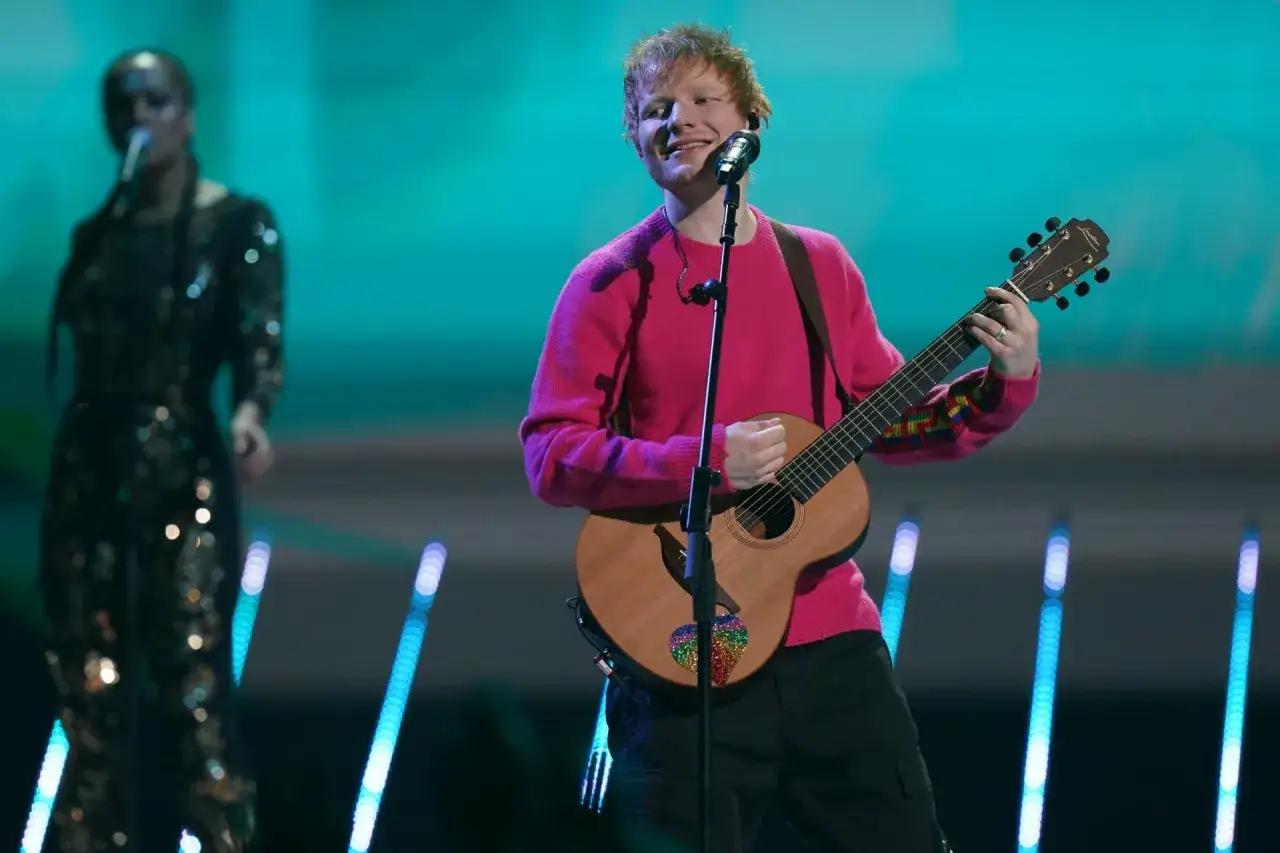 Ed Sheeran w różowym swetrze gra na gitarze. Zastanawiasz się, ile Ed Sheeran bierze za koncert?