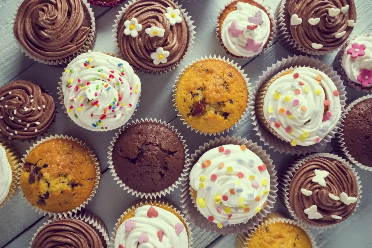 Muffinki czekoladowe kontra babeczki z nadzieniem. Kolorowe posypki i dekoracje na babeczkach tworzą apetyczny widok.