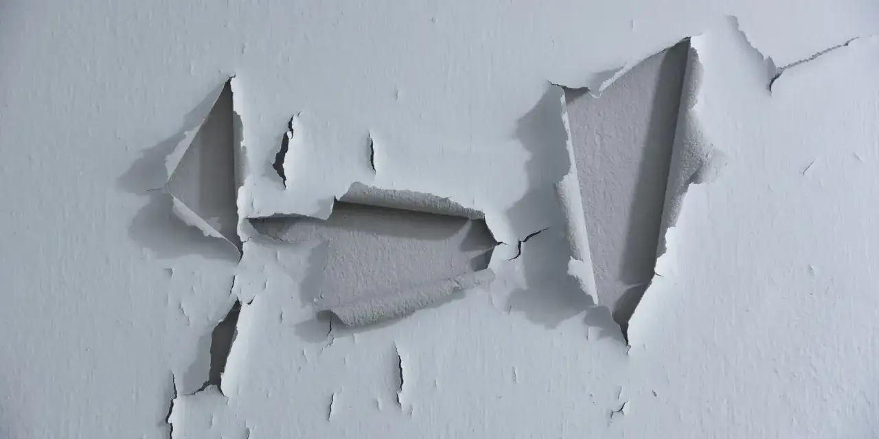 Pintura desconchada revela capas de color gris bajo el blanco.