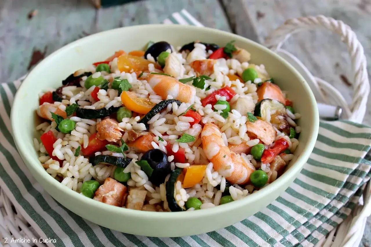 Un'insalata di riso di mare colorata con gamberi, salmone, piselli, pomodorini, olive e zucchine.