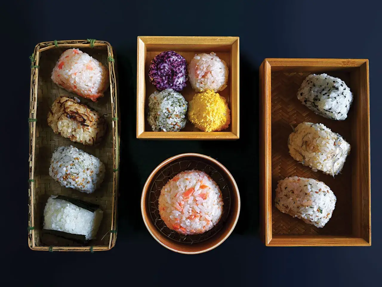 Vielfalt an japanischen Gerichten mit Reis: bunte Onigiri in K&ouml;rbchen und Schalen, mit Lachs, Algen und Sesam.
