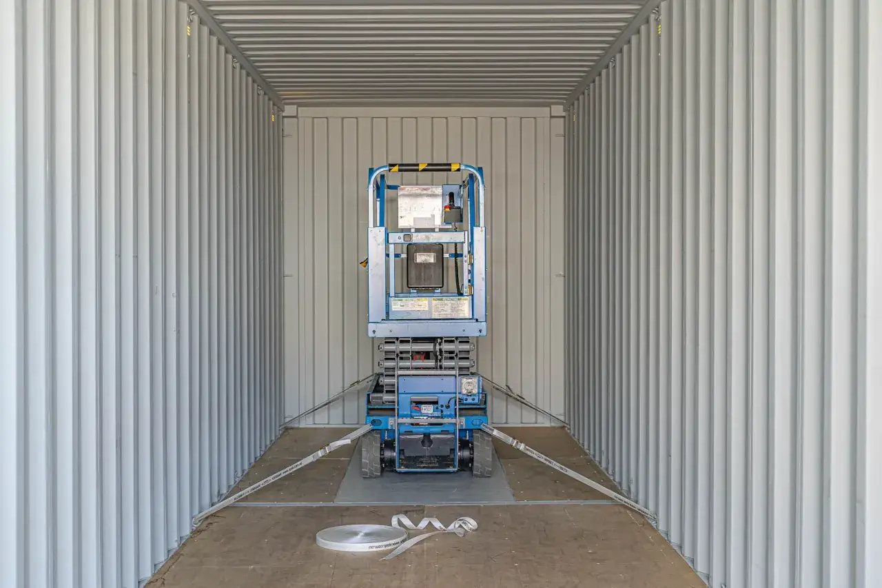 Blauer Hubsteiger im Container, gesichert mit Spanngurten für sicheren Transport. Container lashing ist hier essenziell.