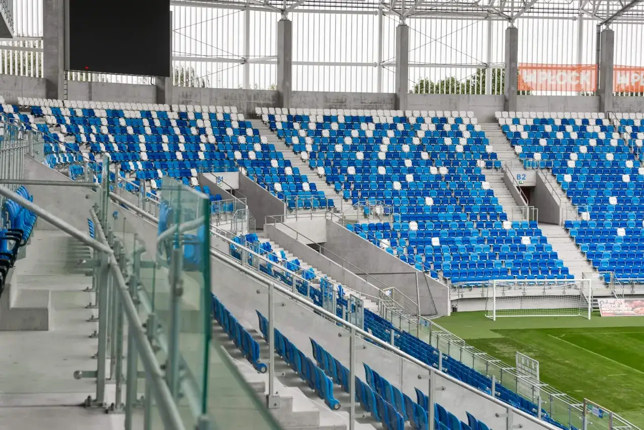 Puste trybuny stadionu Wisły Płock, z rzędami niebieskich i białych krzesełek. Widoczna bramka i fragment murawy.