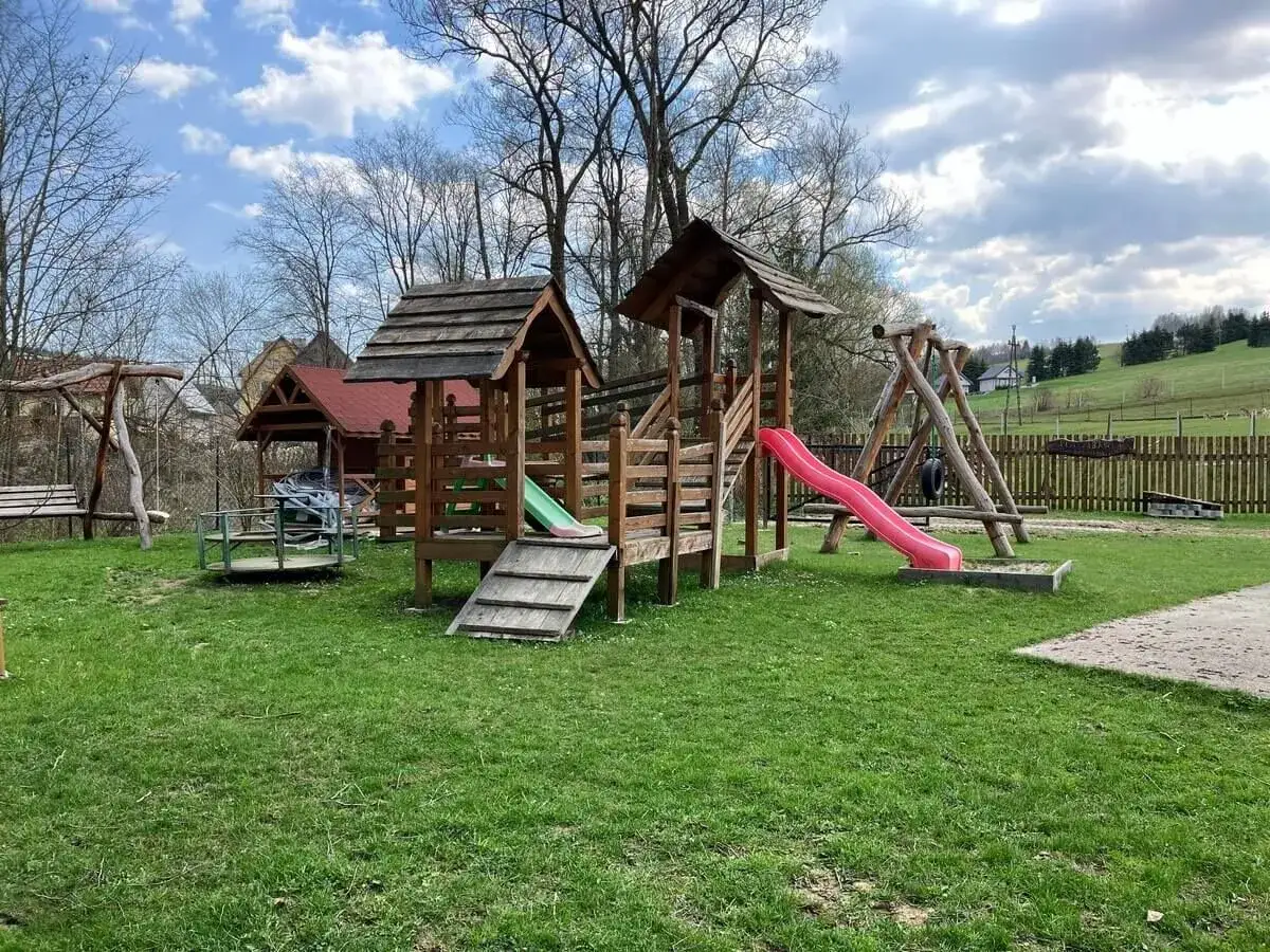 Drewniany plac zabaw z huśtawkami, zjeżdżalniami i karuzelą. Idealne miejsce na podróże z dzieckiem, gdzie maluchy mogą się bawić na świeżym powietrzu.