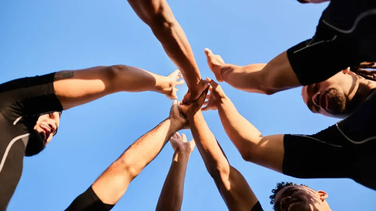 Des mains se rejoignent sous un ciel bleu, symbolisant une idée de challenge sportif et l'esprit d'équipe.