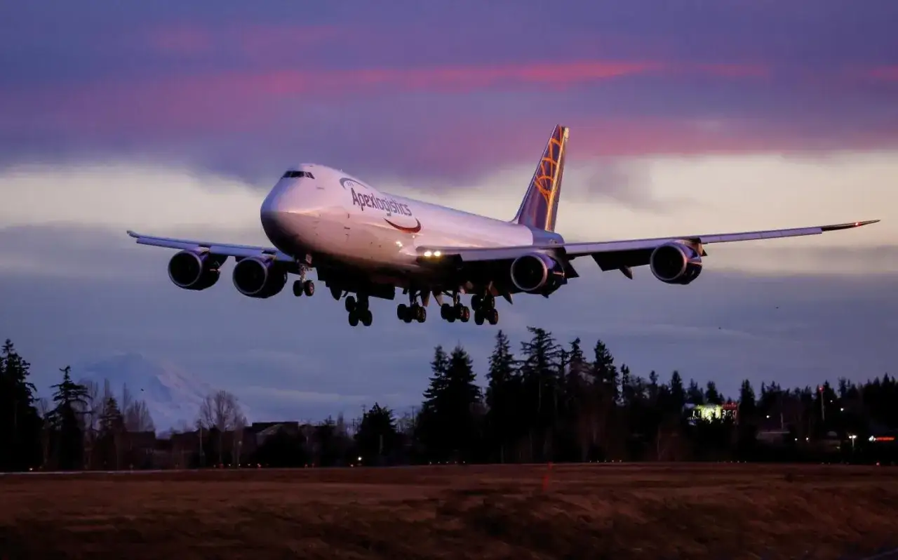 Ein 747 Boeing Frachtflugzeug von Apex Logistics landet bei Sonnenuntergang vor einem Berg.