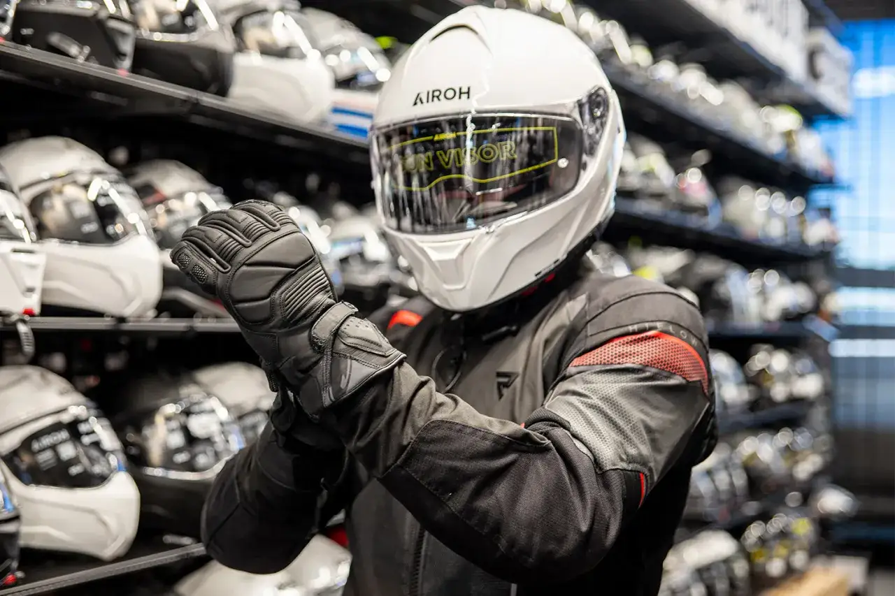 Motocyklista w białym kasku Airoh z szybą przeciwsłoneczną. Czy wiesz, co to jest Pinlock w kasku? To wkładka zapobiegająca parowaniu wizjera.