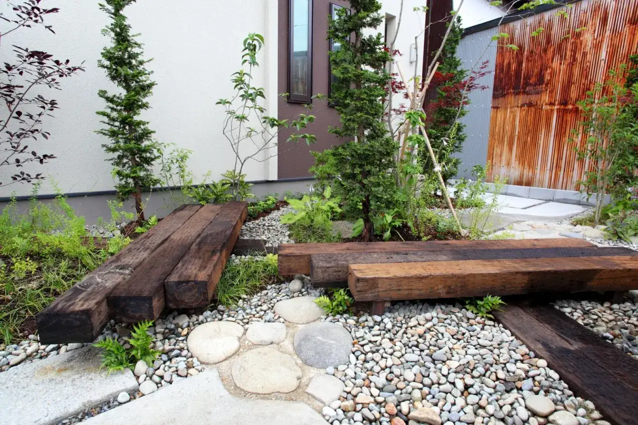 Come abbellire un giardino con pochi soldi: panchine e passerelle in legno riciclato creano un percorso naturale tra ghiaia e piante.
