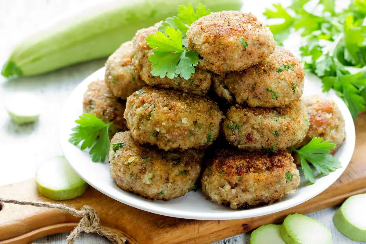 Piatto di polpette di lenticchie dorate, guarnite con prezzemolo fresco. Sullo sfondo, zucchine e fette di limone.