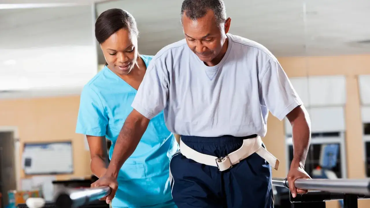 Mann übt unter Anleitung Physiotherapie nach Bobath an parallelbarren.