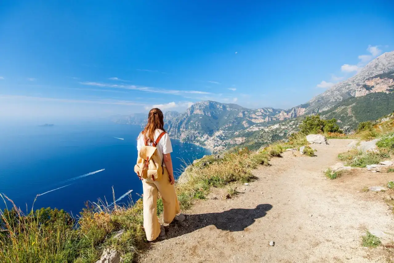 Frau mit Rucksack genie&szlig;t den Ausblick auf die K&uuml;ste Italiens. Ein perfekter Ort f&uuml;r fernwanderwege Italien.