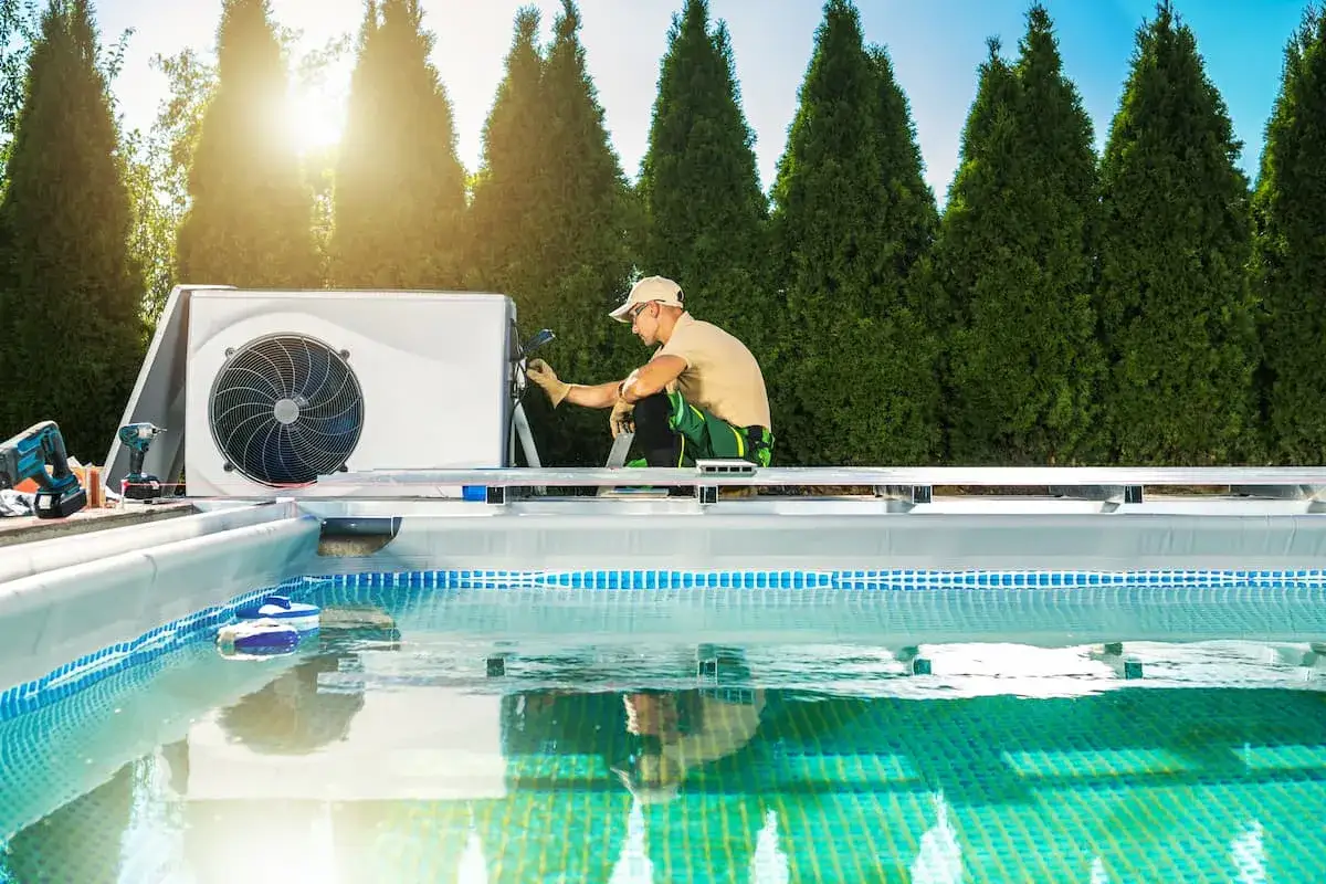T&eacute;cnico instalando unidad de aerotermia para piscinas junto a una piscina con agua cristalina.