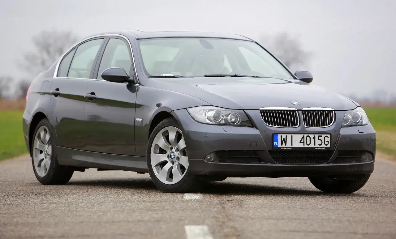 Szare BMW E90 na drodze, z widocznymi reflektorami i grillem.