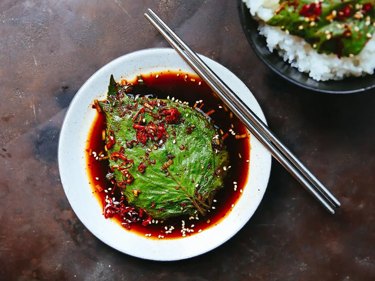 A single shiso leaf, glistening in a dark, savory sauce with chili flakes and sesame seeds, hints at delicious shiso recipes.