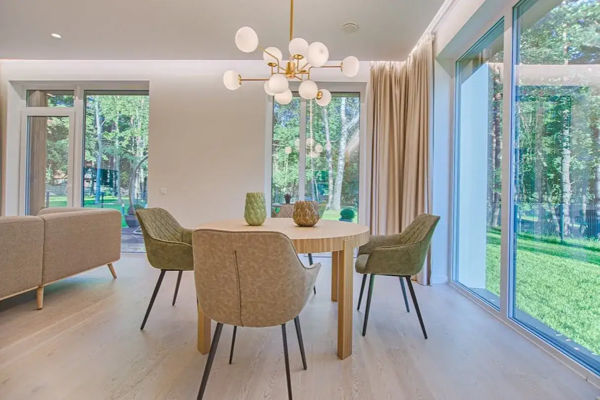 Éclairage salle à manger sans plafonnier : suspension moderne au-dessus d'une table ronde, entourée de chaises vertes. Lumière naturelle abondante.