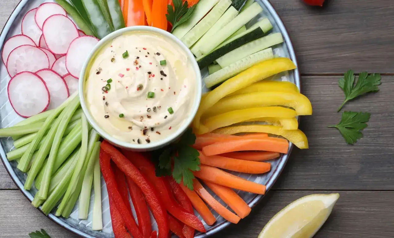 Plato de entrantes saludables con hummus y bastones de verduras: zanahoria, pimiento, pepino, apio y rábano.