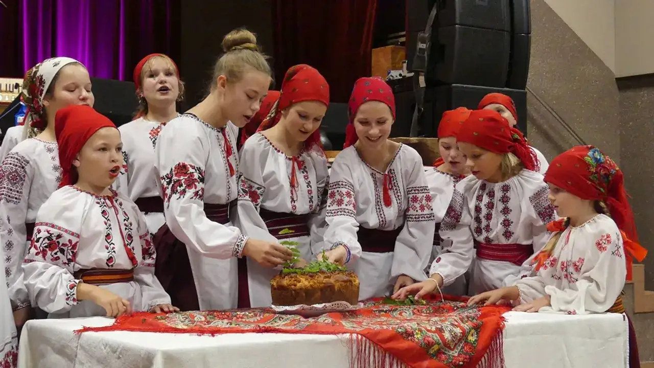 Dzieci w tradycyjnych strojach, prezentujące ukraińską kulturę i tradycje, ozdabiają chleb.
