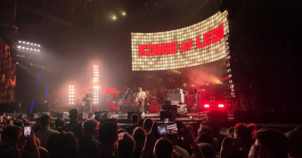 Koncert Kings of Leon na żywo, z zespołem na scenie i wielkim ekranem z napisem