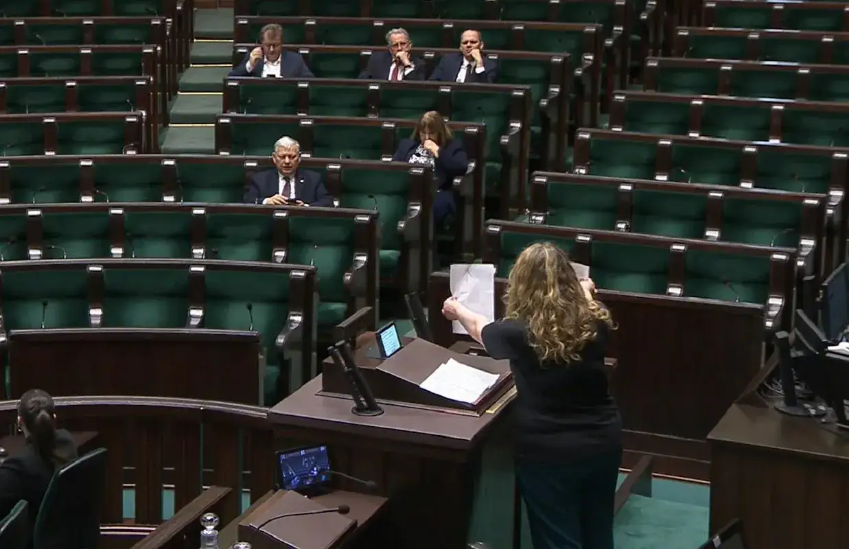 Kobieta przemawia na mównicy, a w ławach siedzą politycy, wśród nich liderzy Konfederacji.