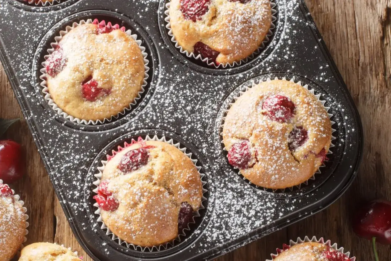 Frisch gebackene Kirsch Muffins, best&auml;ubt mit Puderzucker, in einer Muffinform.