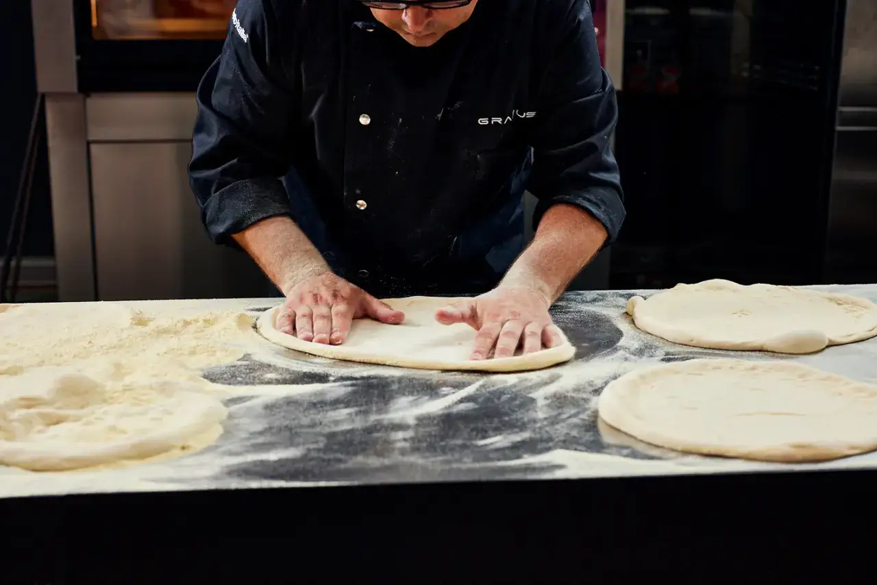 Mani esperte stendono impasti per pizza infarinati. La lievitazione in forno a 40 gradi quanto tempo? Dipende dalla ricetta, ma la pazienza &egrave; la chiave.