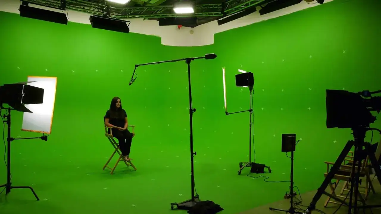 Studio con green screen, luci e microfono. Una donna siede su una sedia, pronta per imparare come si usa il green screen per effetti speciali.