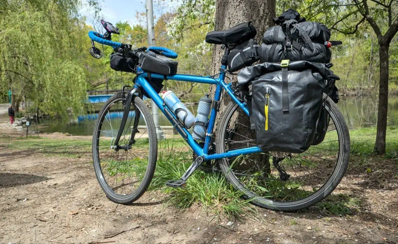 Blå touringcykel med packväskor och all cykel utrustning redo för äventyr vid en sjö.
