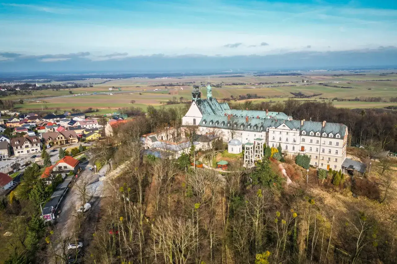Góra Świętej Anny z klasztorem i otaczającą wioską, rozciągająca się na tle pól i nieba.