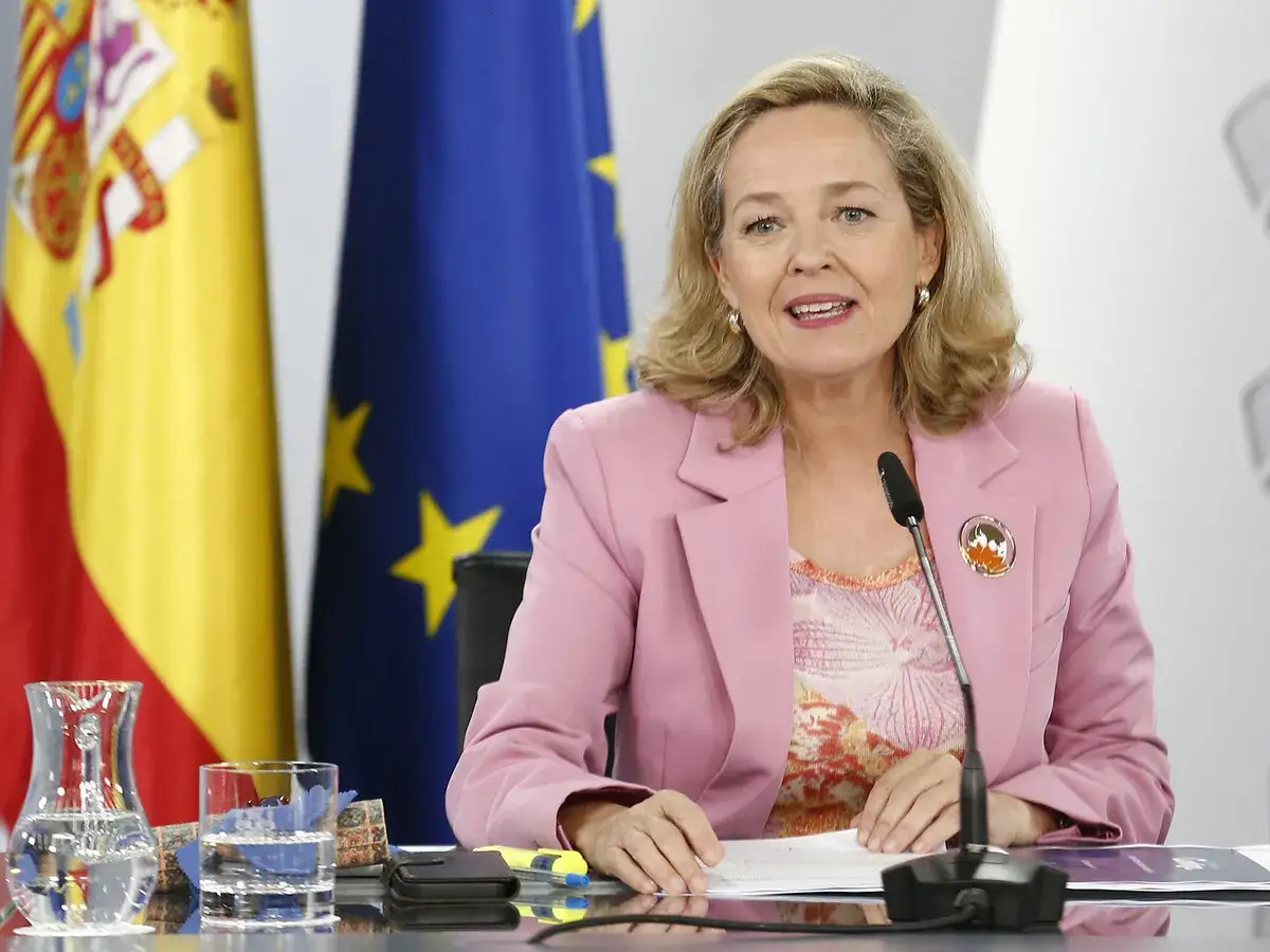 Nadia Calviño, ministra de Economía, habla ante el micrófono. Detrás, las banderas de España y la UE. Es importante recordar que hay que declarar las cuentas corrientes.