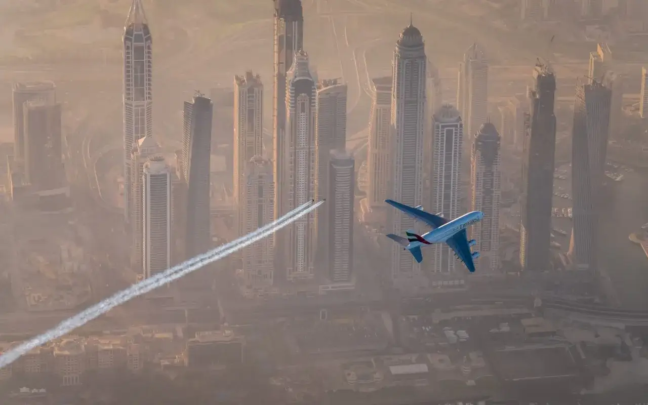 Samolot Emirates leci nad Dubajem, zastanawiasz się, ile trwa lot do Dubaju? Widok na drapacze chmur i niebo.