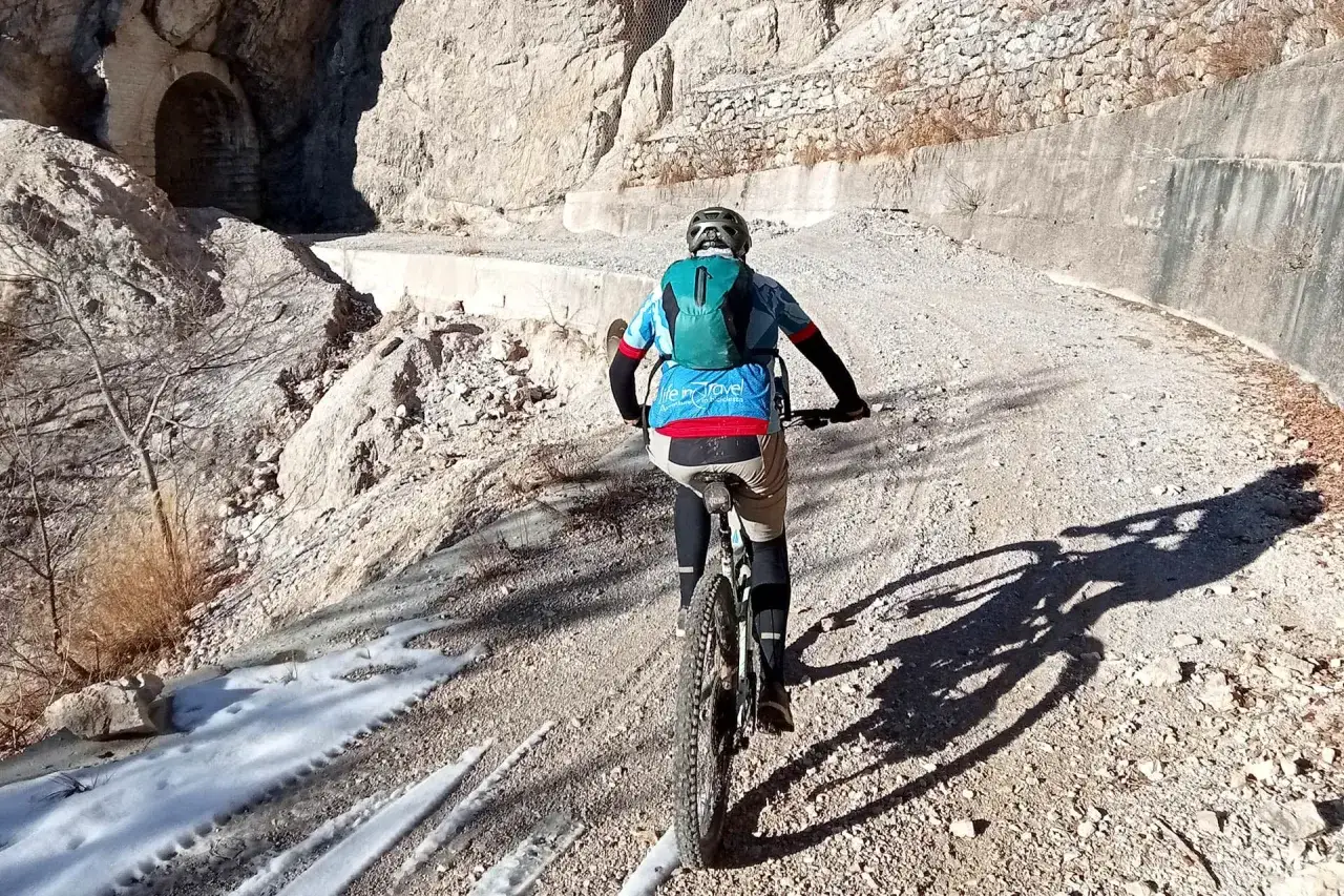 Ciclista pedala su sterrato nel Parco Alto Garda Bresciano, con un tunnel in pietra e rocce a fianco.
