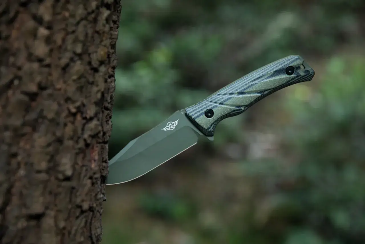 Un cuchillo de supervivencia con mango verde y negro, clavado en un tronco de &aacute;rbol en un bosque.