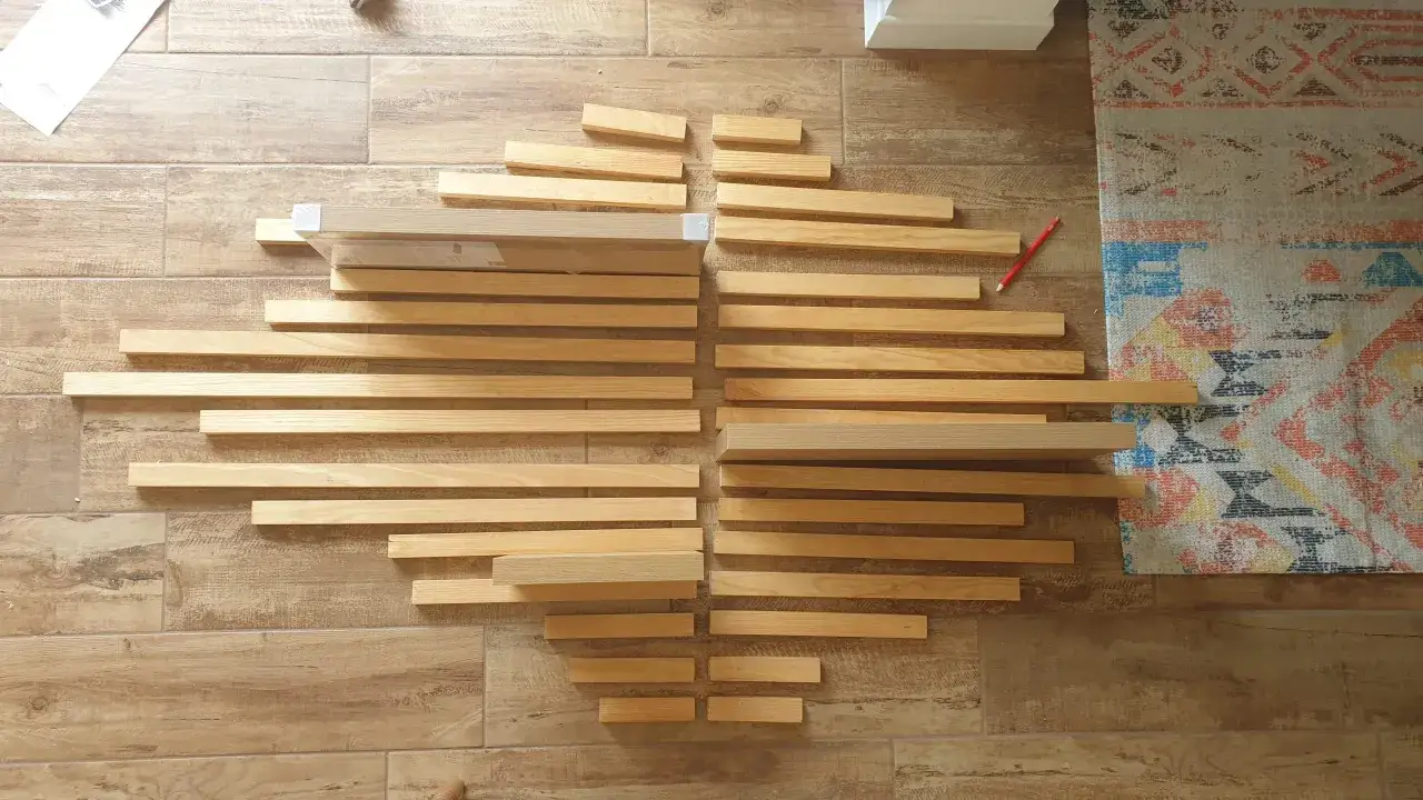 Des planches de bois disposées en éventail, prêtes pour un projet de diy deco murale. Un crayon rouge est posé à côté.