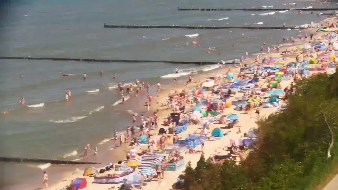 Ustronie Morskie centrum tętni życiem. Tłumy plażowiczów kąpią się w morzu i opalają na piasku wśród kolorowych parawanów i parasoli.