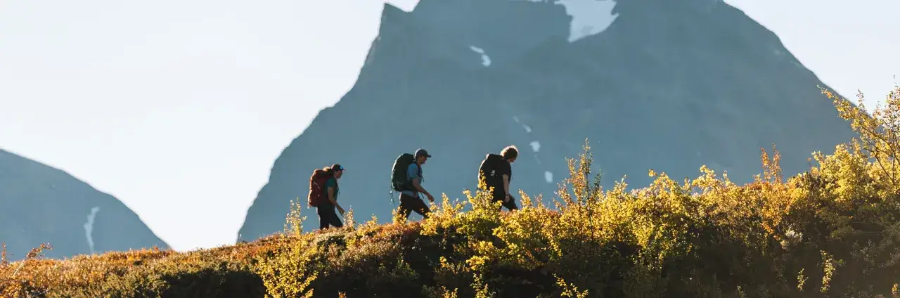 Vandrare p&aring; v&auml;g mot Kebnekaise fr&aring;n Nikkaluokta, med h&ouml;stens f&auml;rger och majest&auml;tiska berg i bakgrunden.
