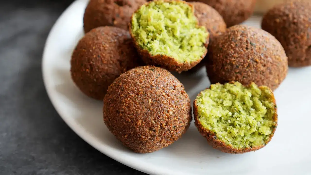 Frisch zubereitete Falafel auf einem Teller. Ein Biss zeigt das leuchtend gr&uuml;ne Innere. Perfekt zum falafel selber machen!