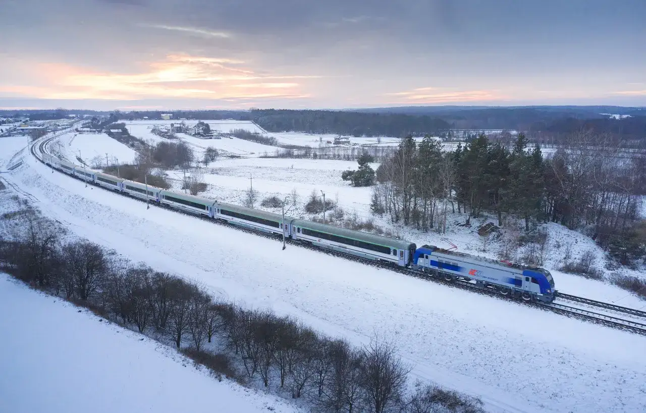Pociąg PKP Intercity jedzie przez ośnieżony krajobraz. Trasa Warszawa Gdańsk w zimowej scenerii.