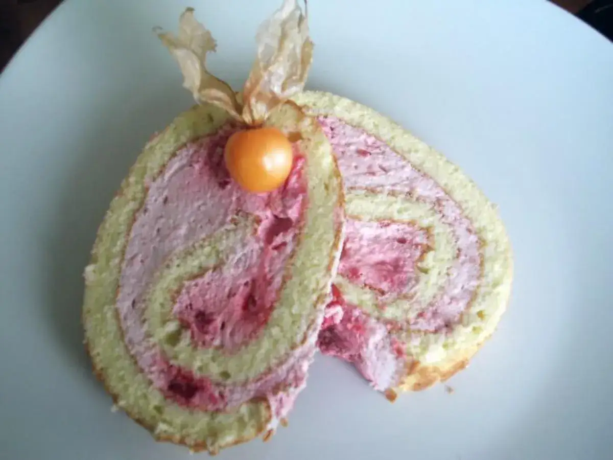 Zwei Scheiben Himbeer Biskuitrolle mit rosa Creme und einer Physalis garniert.