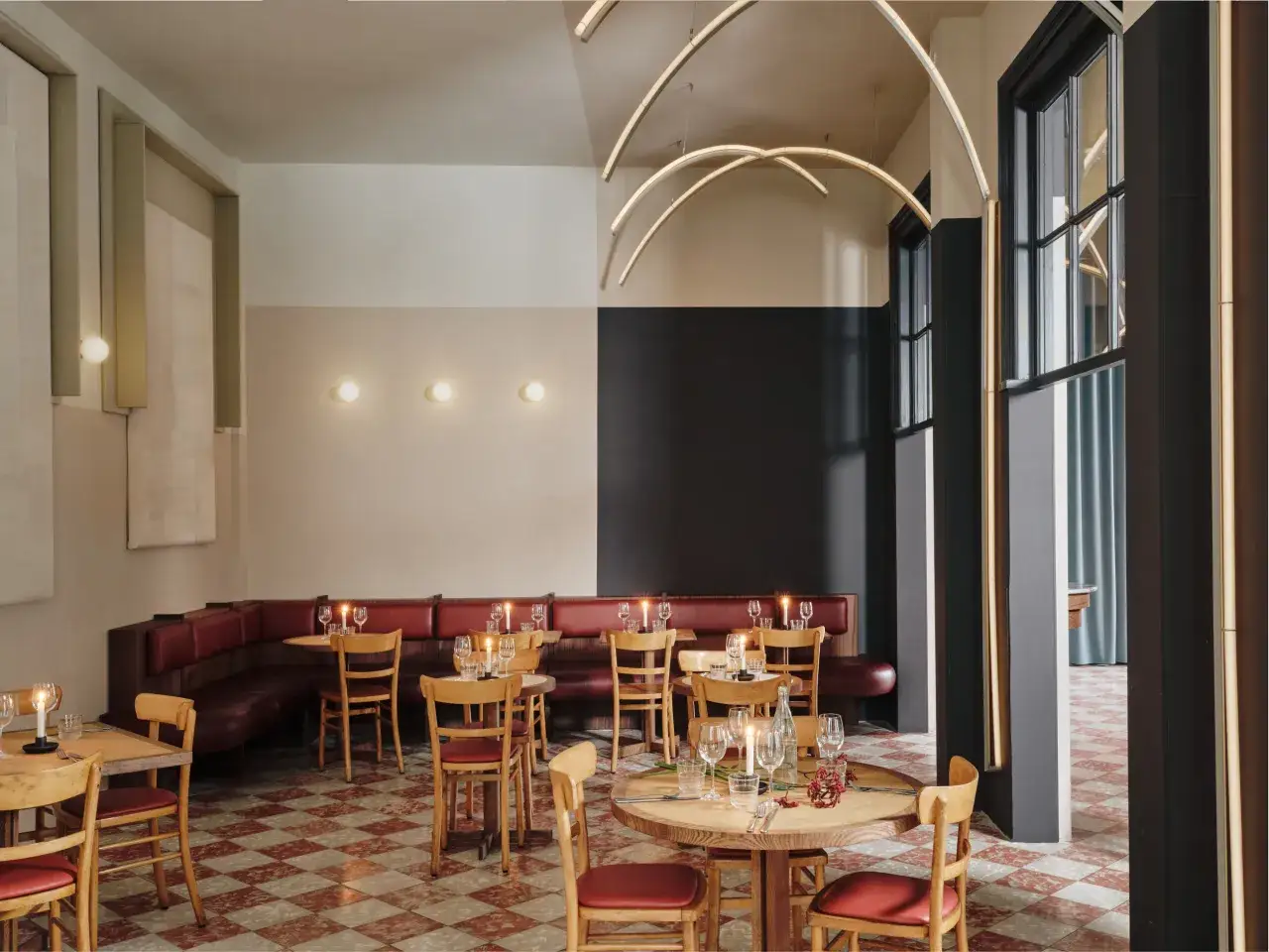 Przytulne wnętrze bistro z czerwonymi skórzanymi kanapami, drewnianymi stołami i krzesłami, ozdobione świecami i nowoczesnym oświetleniem.