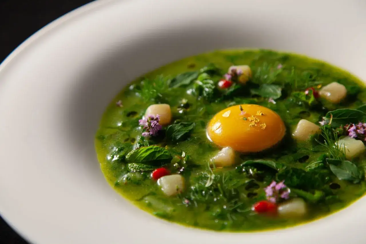 Un piatto verde brillante con tuorlo d'uovo e cubetti bianchi. Un assaggio di Tuscania cosa mangiare: erbe fresche e sapori delicati.