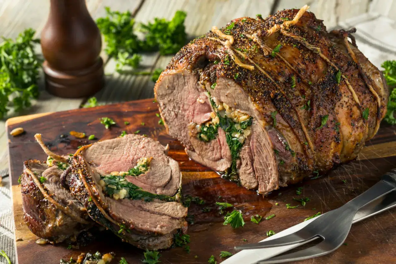 Gigot d'agneau au four, rôti et farci aux herbes, coupé en tranches sur une planche en bois.