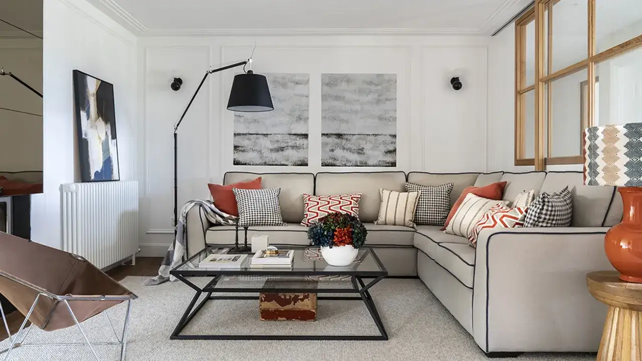 Sof&aacute; rinconera gris, cojines variados y mesa de centro de cristal. Un espacio acogedor para decorar sal&oacute;n.