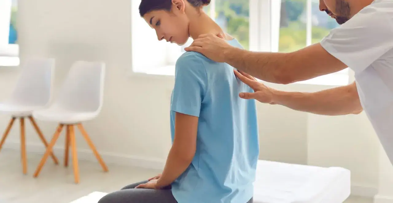 Un kinésithérapeute examine le cou d'une jeune femme, peut-être pour évaluer le temps de guérison d'une hernie cervicale.