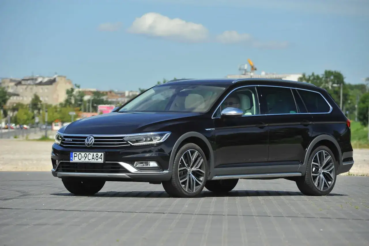 Czarny Passat Alltrack z polskimi tablicami rejestracyjnymi PO-9CA84 zaparkowany na placu.