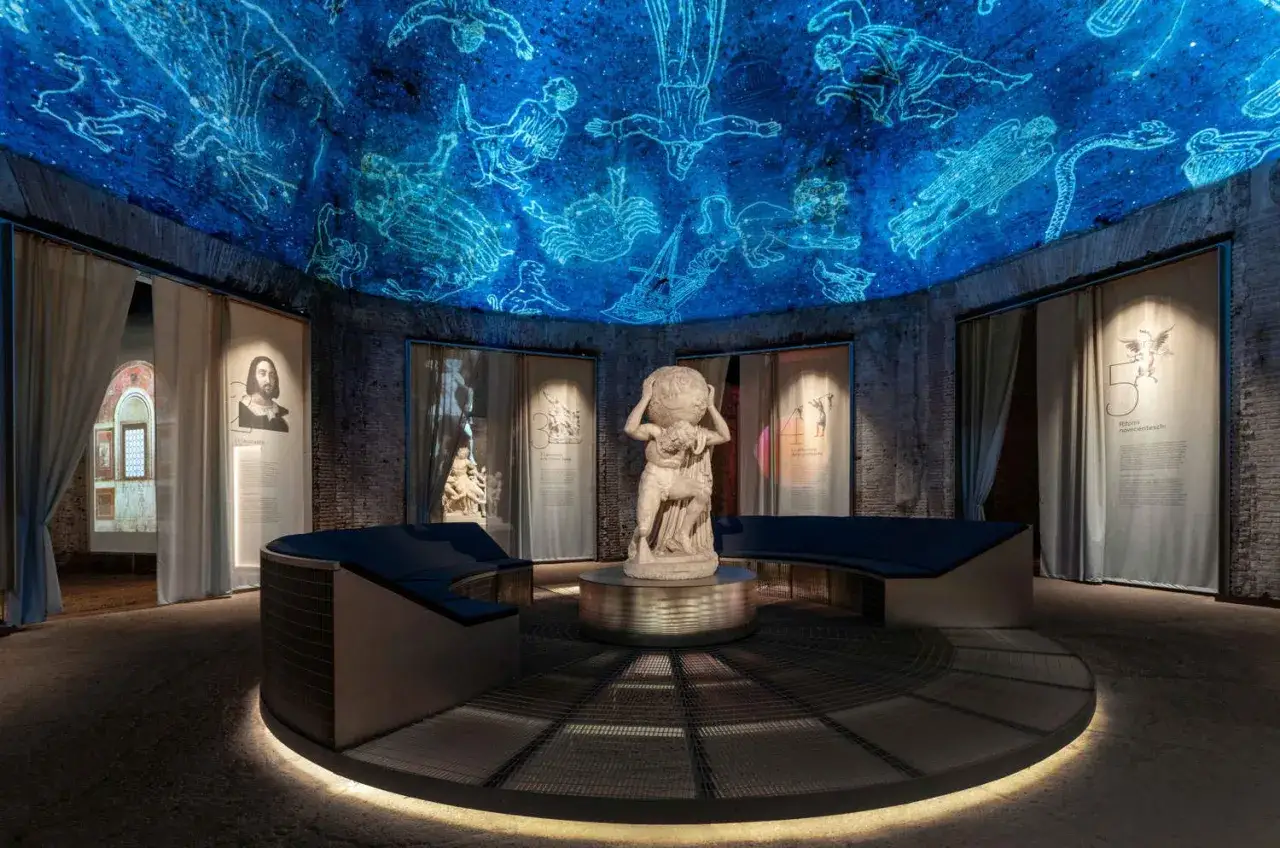 Salle d'exposition avec une fresque céleste projetée au plafond, évoquant la Domus Aurea. Une statue d'Atlas trône au centre.